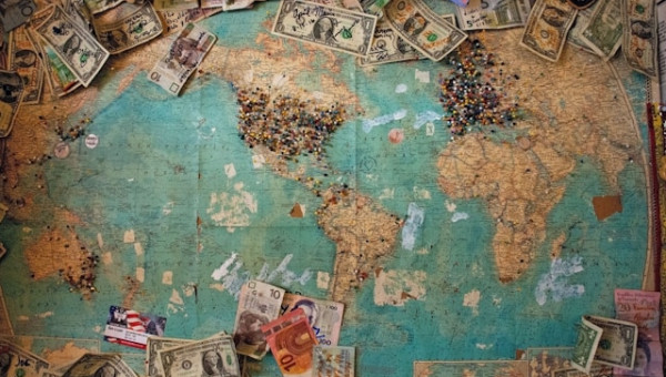 Dargestellt ist eine Weltkarte mit angepinnten Geldscheinen und Stecknadeln