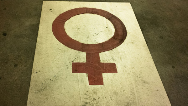 Das Bild stellt ein auf die Straße gezeichnetes Weiblichkeitszeichen in rot auf weißem Grund dar